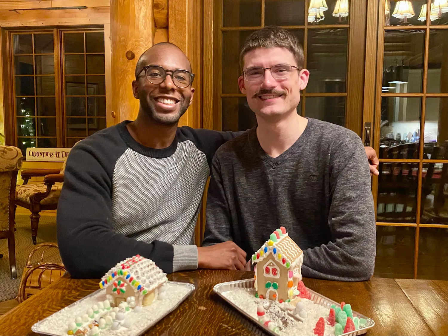 Picture of myself with my husband posing behind our gingerbread houses at Christmas